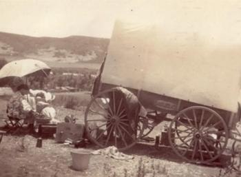 Madonna Ahrens doing laundry outside San Diego beside a covered wagon, June 1906